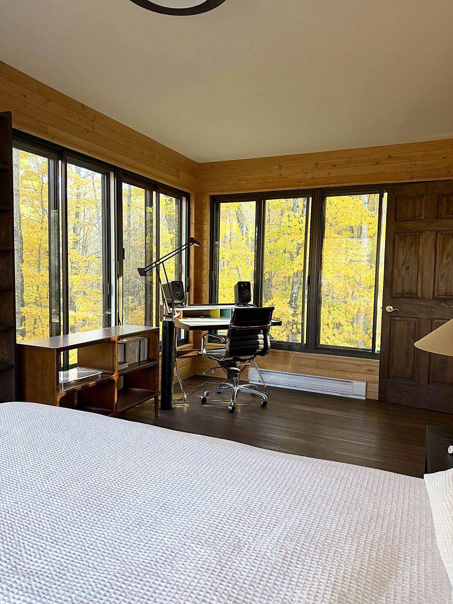 La chambre principale avec le bureau dans l’angle, la forêt jaune derrière les fenêtres.
