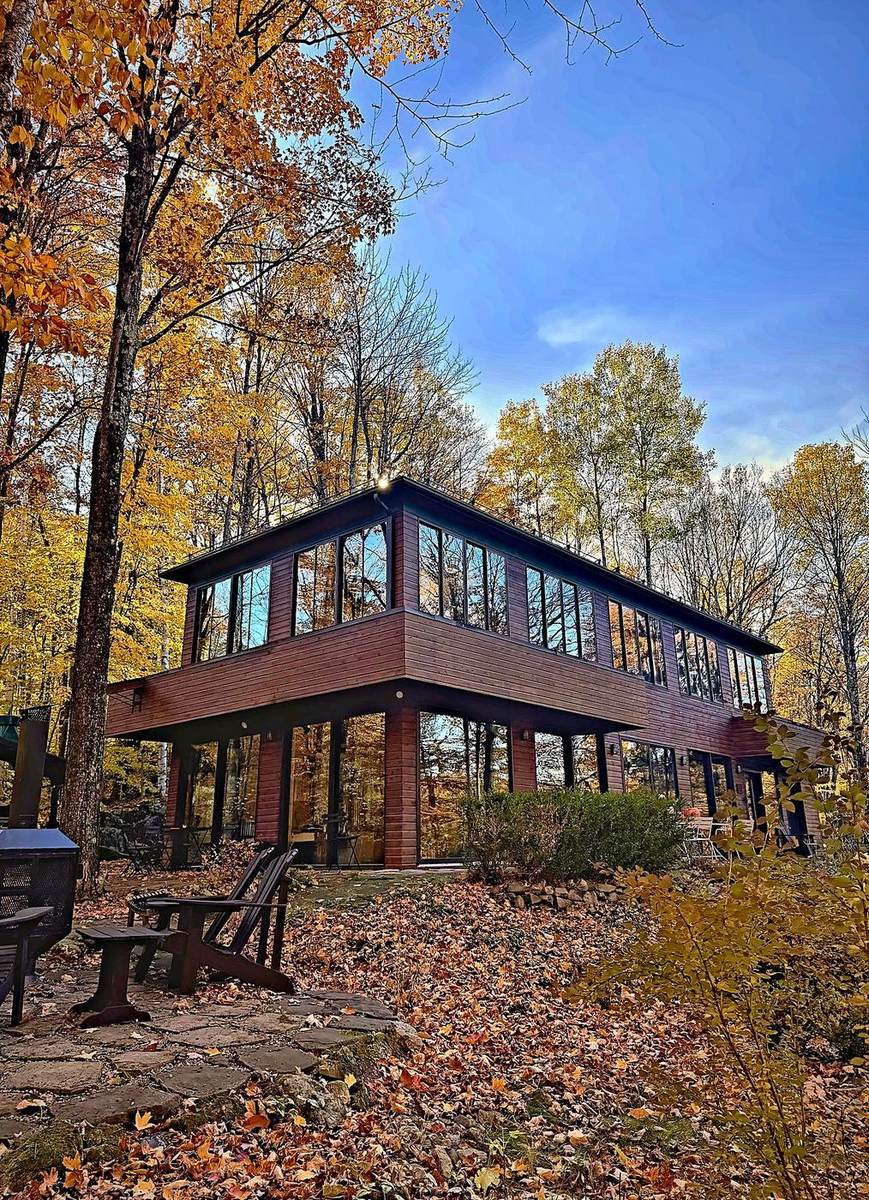 BOSCO à l’automne : le chalet en bois et ses longues fenêtres, au milieu des érables dorés.