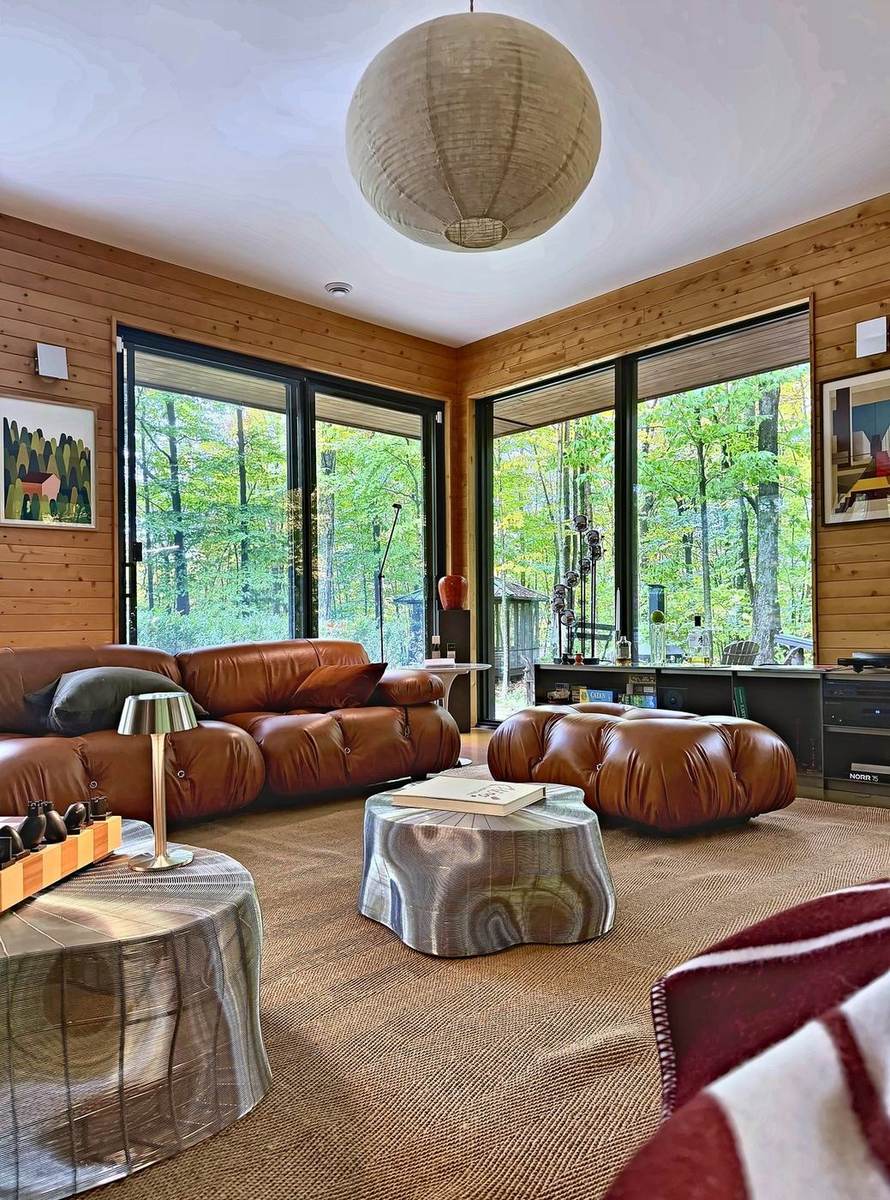 Le salon : canapés en cuir cognac, lanterne de papier et grandes fenêtres sur la forêt.